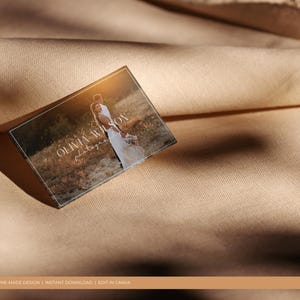 May include: A business card with a white border and a light brown background. The text "Olivia Wilson Photography" is printed in white on the card. A photo of a couple in a field is in the background.