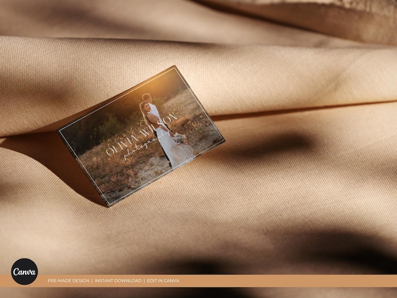 May include: A business card with a white border and a light brown background. The text "Olivia Wilson Photography" is printed in white on the card. A photo of a couple in a field is in the background.