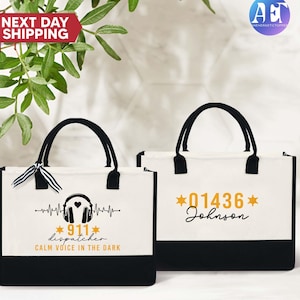 May include: Two white canvas tote bags with black handles. The bag on the left has a black and white graphic of a headset with a heartbeat line and the text "*911* dispatcher CALM VOICE IN THE DARK". The bag on the right has the text "*01436* Johnson" in gold.