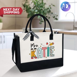 May include: White canvas tote bag with black handles and a black bottom. The bag has a colorful design with the text "Mrs. Katie" and school-themed illustrations.