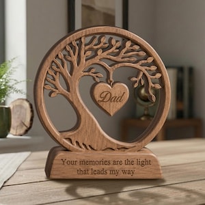 May include: A circular wooden ornament featuring a laser-cut tree design with a heart-shaped pendant in the centre engraved with the word Dad. The base is rectangular and engraved with the text Your memories are the light that leads my way.