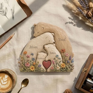 K&ouml;nnte beinhalten: Eine geschnitzte Holzskulptur einer B&auml;renfamilie. Die Skulptur zeigt eine Mutter, einen Vater und zwei Jungtiere, mit den Namen "Mom", "Dad", "John" und "Ashley". Ein rotes Herz befindet sich in der Mitte. Die B&auml;ren sind von bunten Blumen umgeben.