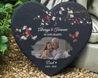 Op de afbeelding: Zwarte, hartvormige leisteen gedenkplaat met een foto van een vader en dochter. De lei heeft witte tekst: "Always & Forever IN OUR HEARTS" en "Dad 1955-2026". Rode kardinalen en witte bloemen sieren de plaat.