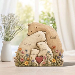 K&ouml;nnte beinhalten: Eine B&auml;renskulptur f&uuml;r die Familie mit den Worten "Mom", "Dad", "Ashley" und "John" in die B&auml;ren geschnitzt. Die Skulptur zeigt ein Herz und ist von bunten Blumen umgeben. Die B&auml;ren sind in Braun- und Cremet&ouml;nen gehalten.