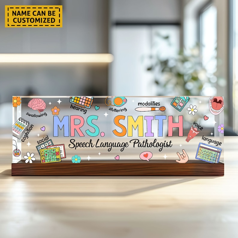May include: A clear acrylic desk nameplate with a wooden base. The nameplate features colorful illustrations of speech therapy related icons and the text "MRS. SMITH Speech Language Pathologist".