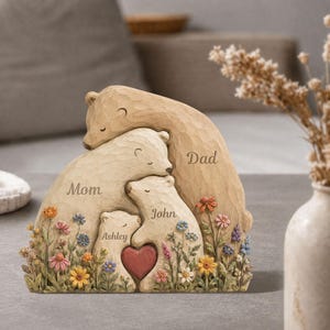K&ouml;nnte beinhalten: Eine geschnitzte Holzskulptur einer B&auml;renfamilie mit den Worten "Mom", "Dad", "John" und "Ashley". Die B&auml;ren sind von bunten Blumen und einem roten Herzen umgeben.