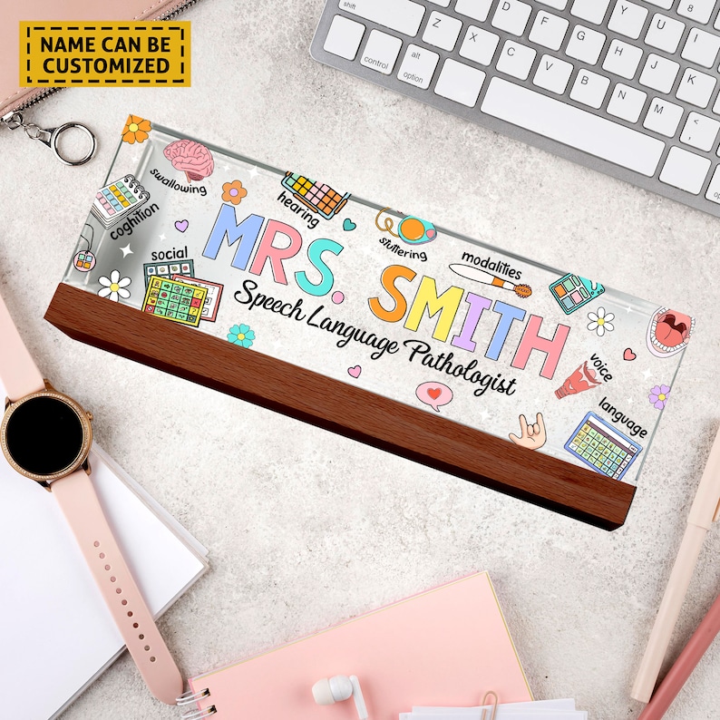 May include: A personalized desk nameplate with a clear acrylic base and a wooden stand. The nameplate features a colorful design with speech therapy related icons and the text "MRS. SMITH Speech Language Pathologist".
