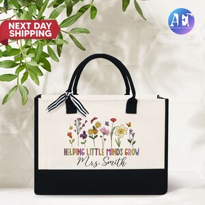 Może przedstawiać: Biała torba typu tote z pł&oacute;tna z czarnymi uchwytami i czarnym dnem. Torba ma kolorowy wz&oacute;r kwiatowy i napis "Helping Little Minds Grow Mrs. Smith".
