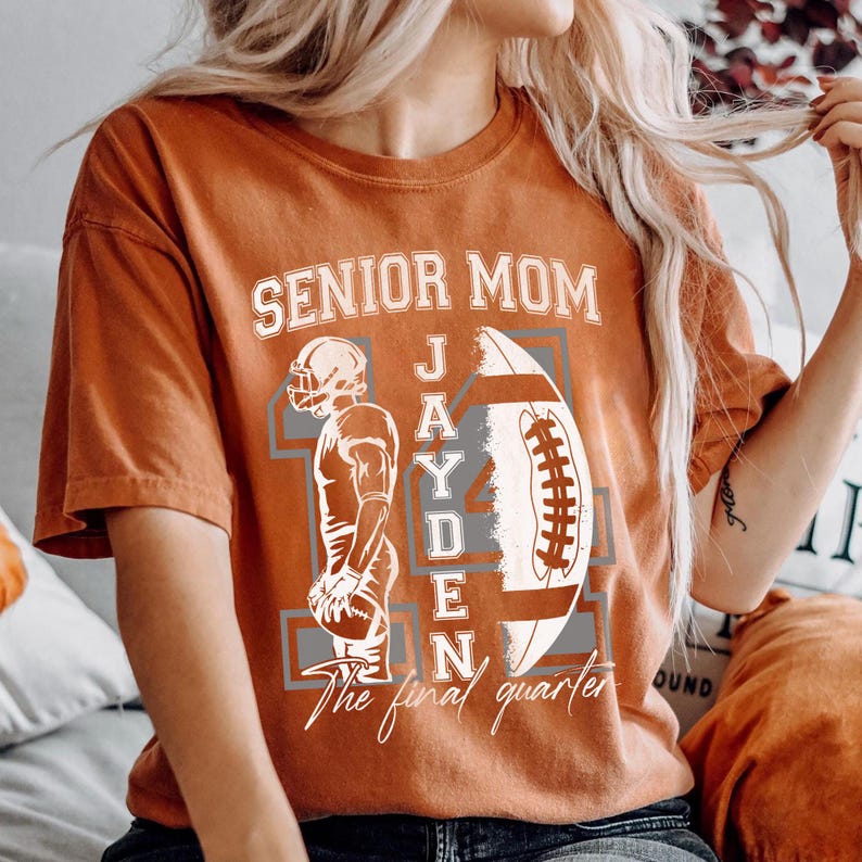 May include: Burnt orange t-shirt with the text "SENIOR MOM" above a football graphic and the name "JAYDEN". A football player graphic is on the left side of the football. The text "The final quarter" is below the football graphic.
