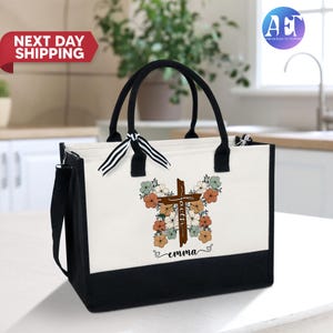 May include: A white canvas tote bag with black trim and handles. The bag features a floral design with a wooden cross in the center. The text "faith" is written on the cross and the name "emma" is written below the cross.