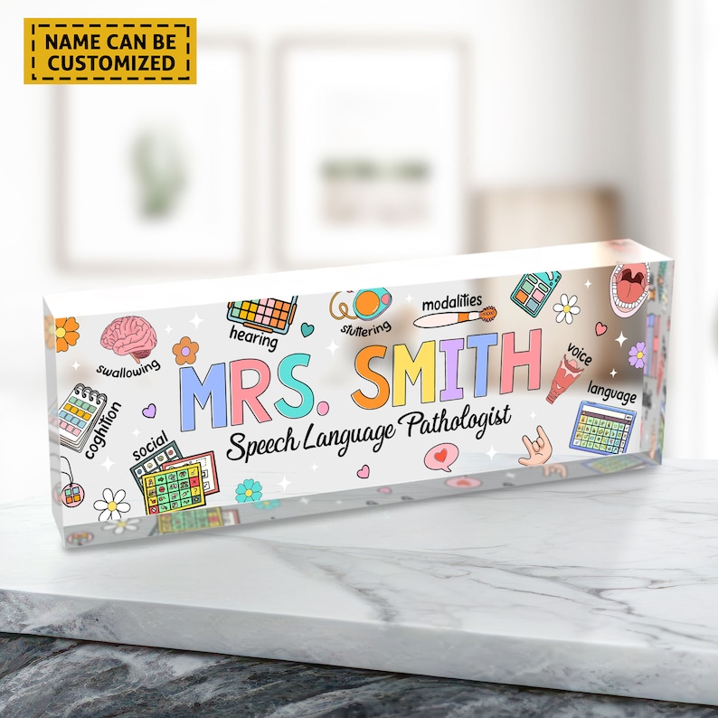 May include: A colorful acrylic desk sign with the text "MRS. SMITH Speech Language Pathologist" and various illustrations related to speech therapy, including a brain, a mouth, a hearing aid, and a speech bubble.
