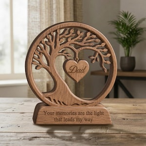 May include: A circular wooden ornament featuring a laser-cut tree design with a heart-shaped pendant hanging from the branches. The heart is engraved with the word Dad. The base is engraved with the text: Your memories are the light that leads my way.