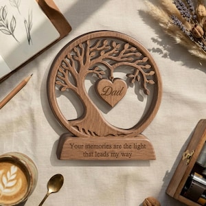 May include: A circular wooden ornament featuring a laser-cut tree design with a heart-shaped pendant in the centre engraved with the word "Dad". The base is engraved with the text "Your memories are the light that leads my way".
