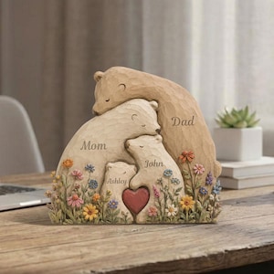 K&ouml;nnte beinhalten: Eine geschnitzte B&auml;renfamilien-Skulptur mit den Worten "Mama", "Papa", "Ashley" und "John". Die Skulptur zeigt ein Herz und bunte Blumen. Die B&auml;ren sind in Beige- und Braunt&ouml;nen gehalten.