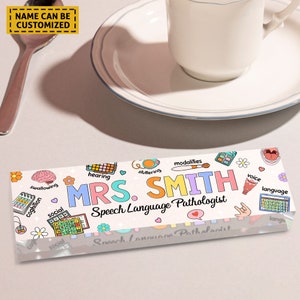 May include: A white acrylic desk plaque with colorful illustrations of speech therapy related icons and the text "MRS. SMITH Speech Language Pathologist".