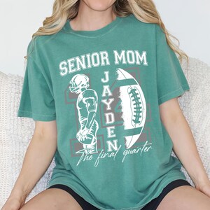May include: Green t-shirt with the text "SENIOR MOM" above a football graphic and the name "JAYDEN". A football player illustration is on the left. The words "The final quarter" are below the football.