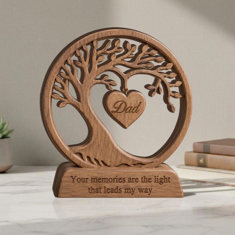 May include: A circular wooden ornament featuring a laser-cut tree design with a heart-shaped pendant in the centre engraved with the word Dad. The base is rectangular and engraved with the text Your memories are the light that leads my way.