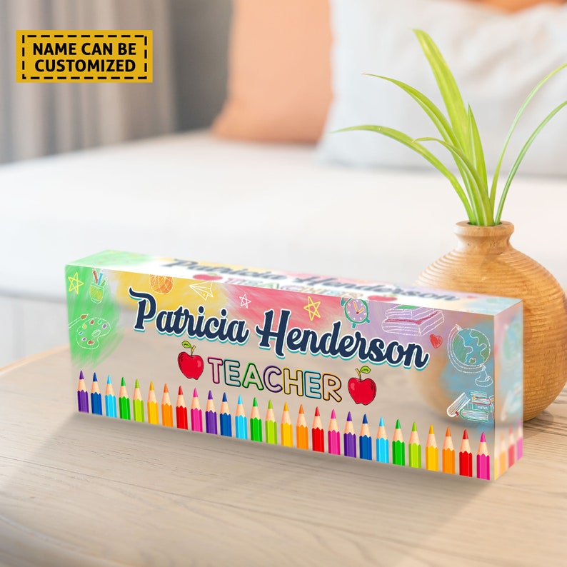 Może przedstawiać: Przezroczysty blok akrylowy z tęczowym tłem tie-dye i kolorowymi oł&oacute;wkami na dole. Tekst "Patricia Henderson TEACHER" jest napisany na bloku niebieskim kolorem. Blok leży na drewnianej powierzchni.