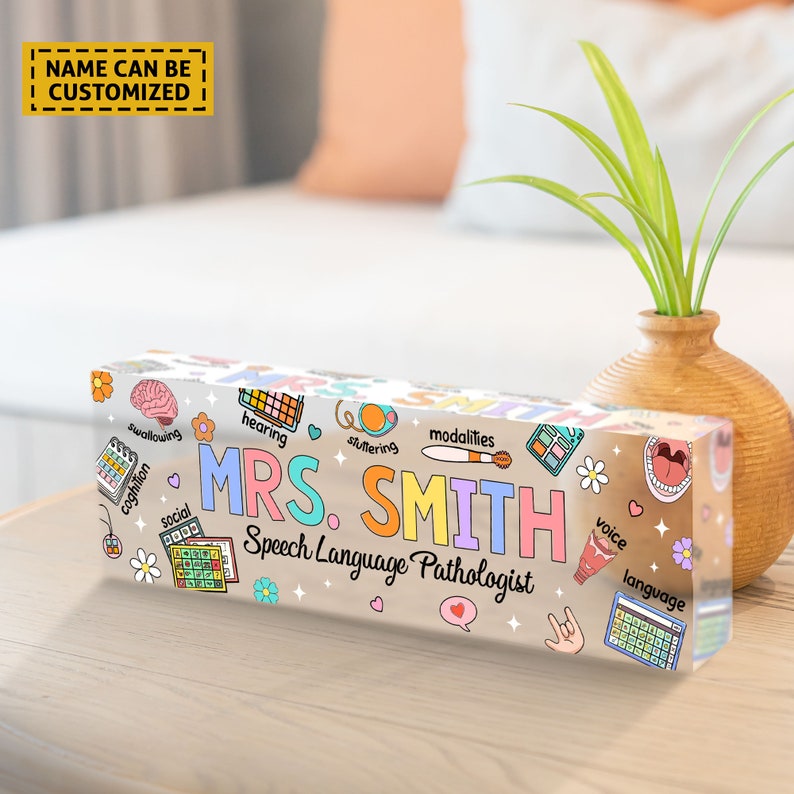 May include: A clear acrylic desk nameplate with a colorful design featuring speech therapy related icons and the text "MRS. SMITH Speech Language Pathologist".