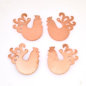 May include: Four copper rooster charms with a cutout design. The charms are a light copper color and have a detailed design.