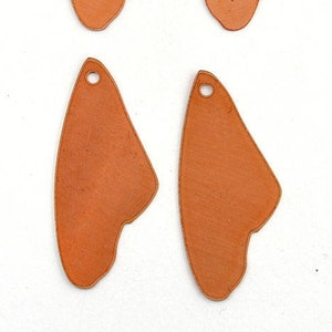 May include: Four copper-colored metal butterfly wing shapes with a hole at the top for hanging. The wings are irregular and have a slightly textured surface.