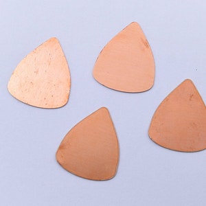 May include: Four copper guitar picks in a teardrop shape, arranged on a white background.