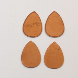 May include: Four teardrop-shaped leather pieces in a light brown color. The pieces are arranged in two rows of two, with the top row slightly offset from the bottom row.