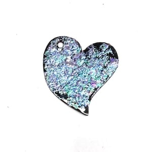 May include: A heart-shaped pendant made of iridescent glass with a hole at the top for hanging. The glass has a blue and green color with a textured surface.