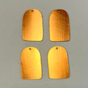 May include: Four gold-colored metal tags with rounded edges and a hole at the top. The tags have a brushed finish.