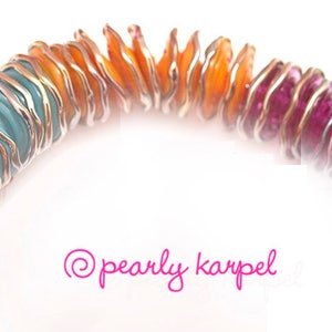 May include: A rainbow-colored glass bead necklace with silver wire wrapping. The beads are layered and have a wavy, organic shape. The colors transition from teal to orange to pink.