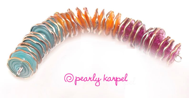 May include: A rainbow-colored glass bead necklace with silver wire wrapping. The beads are layered and have a wavy, organic shape. The colors transition from teal to orange to pink.
