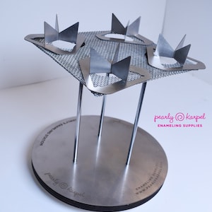 Puede incluir: Un soporte de esmaltado plateado con cuatro soportes met&aacute;licos y una base de malla. El soporte est&aacute; dise&ntilde;ado para sostener cuatro piezas peque&ntilde;as de esmalte para la cocci&oacute;n. El soporte est&aacute; etiquetado "pearly@karpel ENAMELING SUPPLIES".