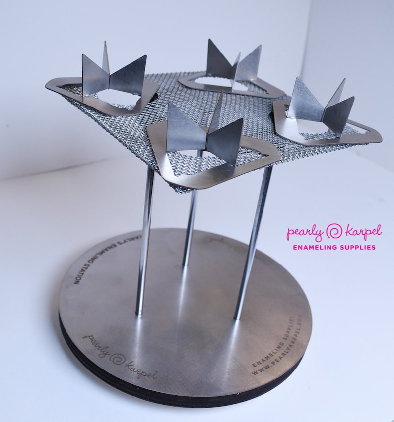 Puede incluir: Un soporte de esmaltado plateado con cuatro soportes met&aacute;licos y una base de malla. El soporte est&aacute; dise&ntilde;ado para sostener cuatro piezas peque&ntilde;as de esmalte para la cocci&oacute;n. El soporte est&aacute; etiquetado "pearly@karpel ENAMELING SUPPLIES".