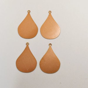 May include: Four teardrop-shaped metal earring blanks, each with a small loop at the top. The blanks are a light copper color.