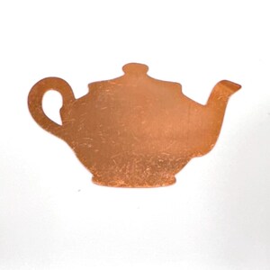 Puede incluir: Recorte de tetera de metal color cobre. La tetera tiene un asa curva, un pico y una tapa. La superficie del metal tiene un aspecto ligeramente texturizado. El recorte está sobre un fondo blanco.