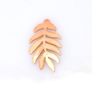 May include: A wooden leaf charm in a light brown color with a hole at the top for hanging. The leaf has a detailed design with multiple veins and a slightly textured surface.