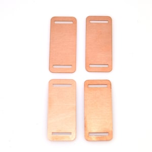 May include: Four rectangular copper-colored metal belt buckles with a smooth finish. Each buckle has two cut-out slots for a belt.