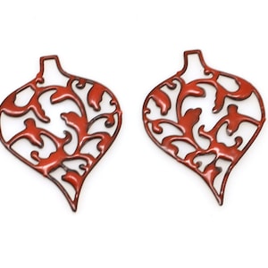Könnte beinhalten: Zwei rote Metall-Weihnachtsbaumschmuckformen mit einem filigranen Design. Die Ornamente sind herzförmig mit einem Wirbelmuster.