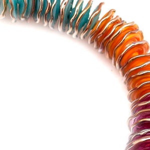 May include: A colorful necklace made of layered, wavy glass beads. The beads are a gradient of teal, orange, and pink.