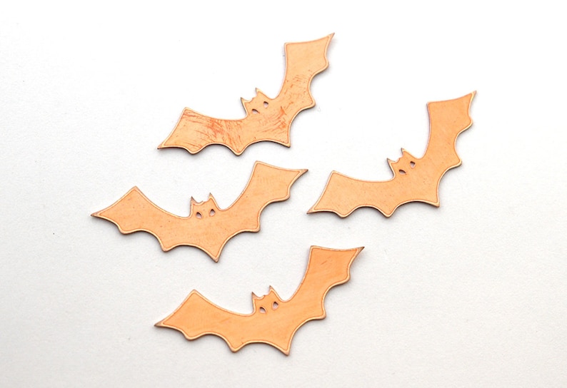 K&ouml;nnte beinhalten: Vier orangefarbene Papierflederm&auml;use mit ausgeschnittenen Augen, auf einem wei&szlig;en Hintergrund angeordnet.
