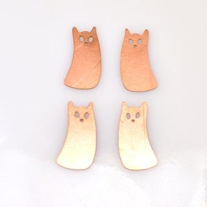May include: Four copper-colored ghost-shaped charms with cut-out eyes. The charms are approximately 2 inches tall and 1 inch wide.