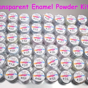 May include: A set of 48 small jars of transparent enamel powder. Each jar has a white label with a number on it. The jars are arranged in a grid pattern on a silver surface.