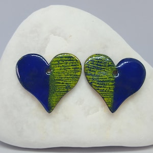 May include: A pair of heart-shaped earrings with a blue and green enamel design. The earrings are on a white stone background.