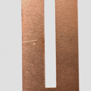 May include: A copper-colored metal rectangle with a rectangular cutout in the center. The metal has a brushed finish.
