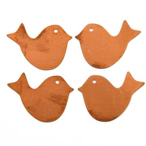 Pode incluir: Quatro pingentes de cobre planos em forma de pássaro dispostos em uma grade dois por dois. Cada peça metálica apresenta uma superfície lisa de cor marrom-avermelhada com um pequeno orifício circular perto do topo para pendurar.