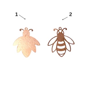 May include: Two copper-colored bee-shaped charms. One is solid, with a textured surface. The other is an openwork design, showing the bee's body and wings. Both have a small loop at the top for hanging, suitable for jewelry making or crafting.