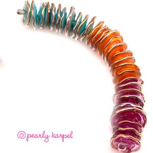 May include: A colorful bracelet made of stacked, scalloped glass beads. The beads are a gradient of turquoise, orange, and pink.
