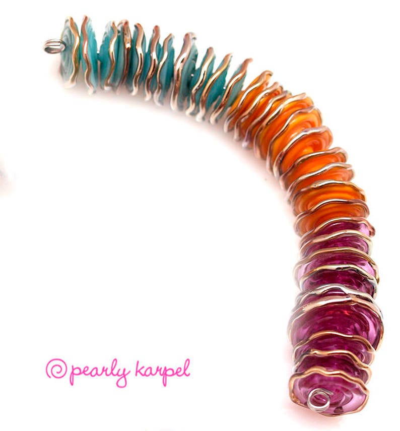 May include: A colorful bracelet made of stacked, scalloped glass beads. The beads are a gradient of turquoise, orange, and pink.