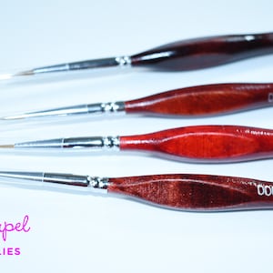 Puede incluir: Conjunto de cuatro pinceles de pintura de detalle con mangos de madera. Los pinceles están etiquetados como 000, 00, 0 y 0. Los pinceles están dispuestos del más grande al más pequeño.