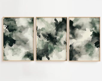 May include: Set of three framed abstract art prints. Each print features a blend of dark green, gray, and white brushstrokes, creating a cloudy or smoky effect. The artwork is encased in a light brown wooden frame, suitable for home decor.